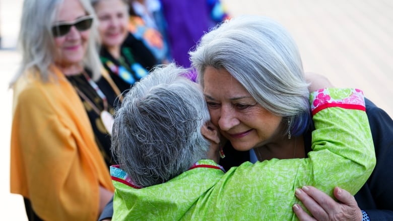 A woman hugs a woman in a green jacket as spectators look on.