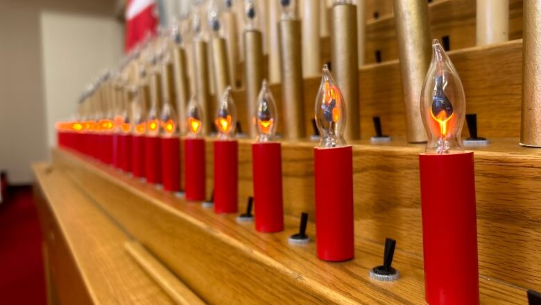 A row of red electric candles on top of a wooden pew inside a church. 