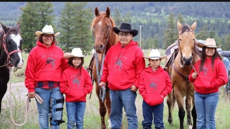 A man, a woman, and three children stand with three horses, wearing matching sweaters and cowboy hats. 