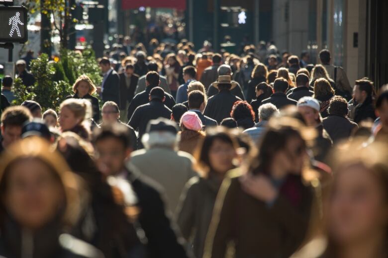 A crowds of people walk along a daytime, city street. 