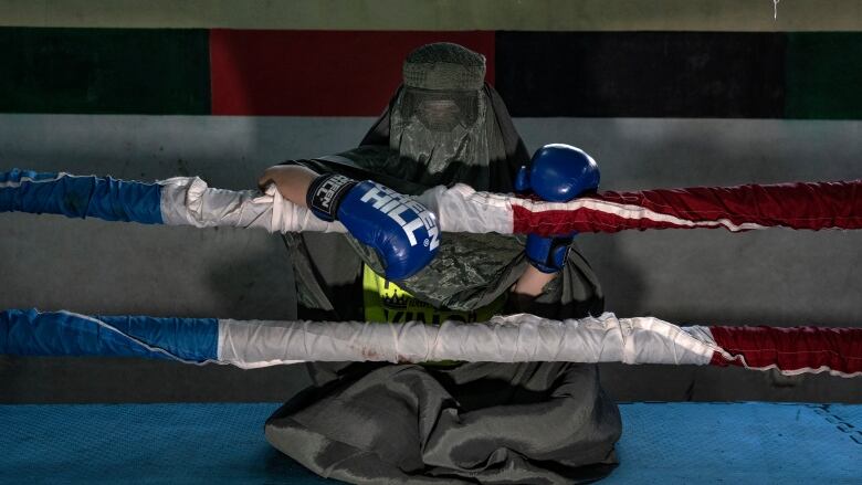 A woman in a burqa kneels in a boxing ring.