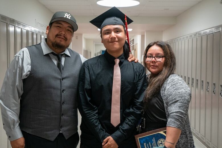 Three people pose in a hallway full of school lockers.