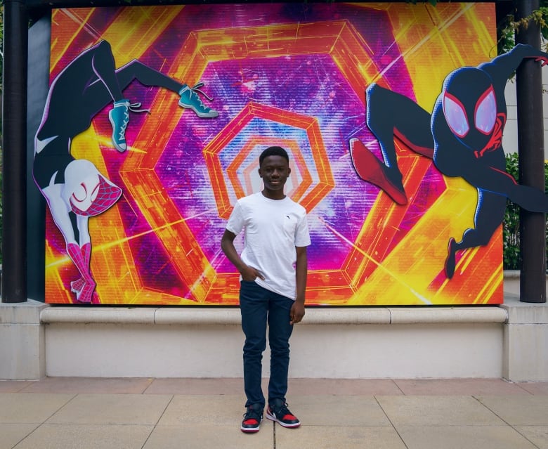 A young man stands in front of a poster 