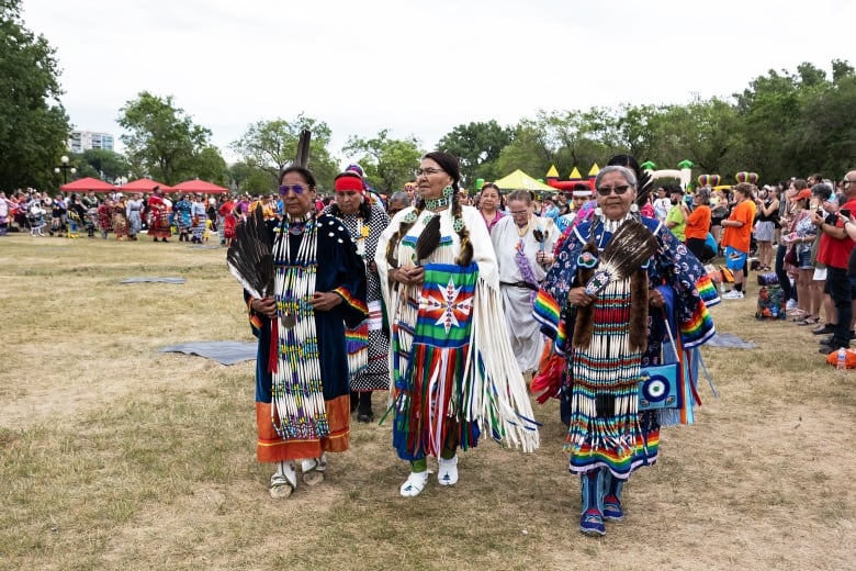 Dancers dressed in traditional regalia enter a powwow. 