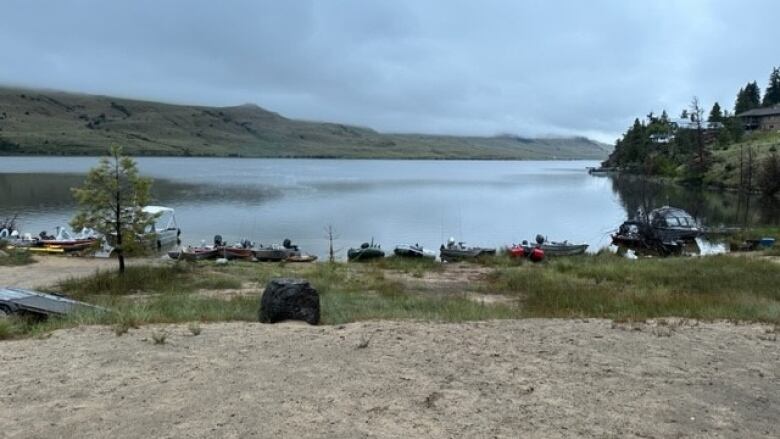 A wide shot of a lakeshore with cars on the sand along the shores of a placid lake framed by hills late on an overcast day.