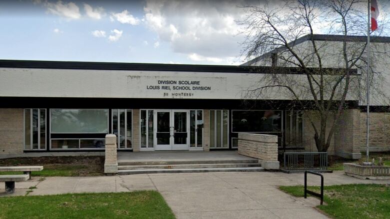 The front of a building is seen from the exterior. A sign above the front doors says Louis Riel School Division. 