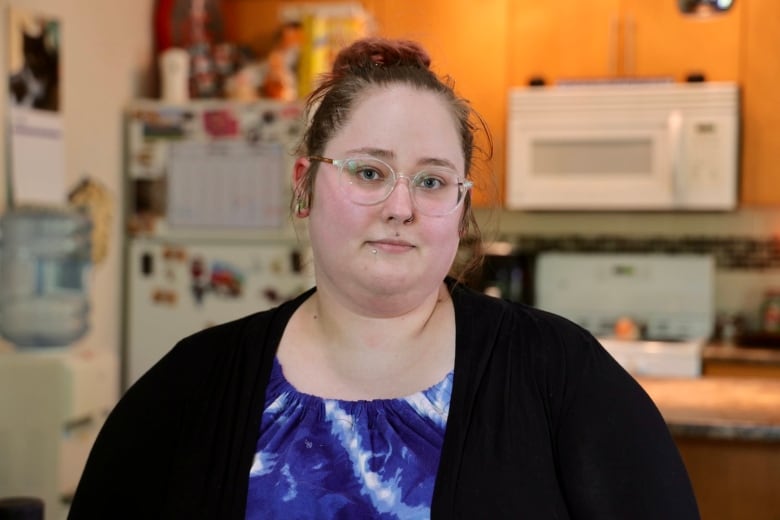 A woman looks at the camera while standing in her apartment