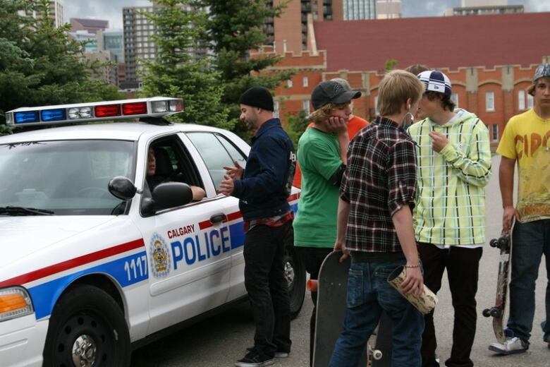 A man talks with police officers through the window of a car while several young men with skateboards stand nearby.