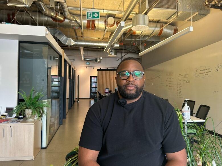 A man sits inside an office, decorated with plants. 