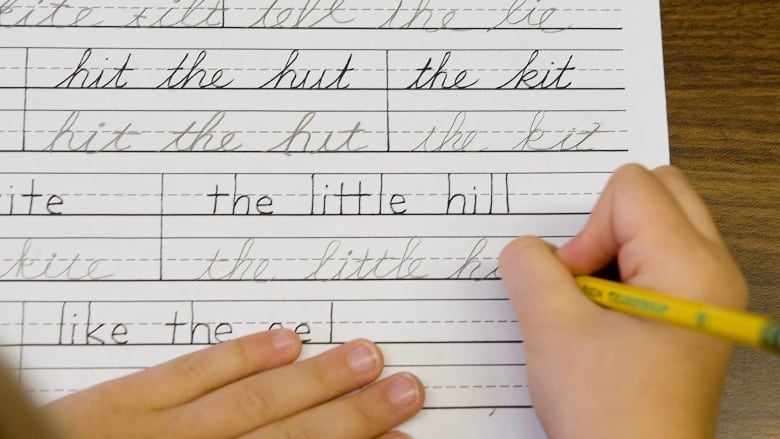 A kid's hands on a piece of paper, holding a pencil and writing in cursive.