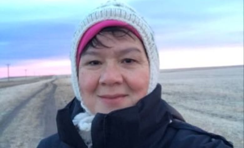 A woman in a toque and coat stands in a wintery field