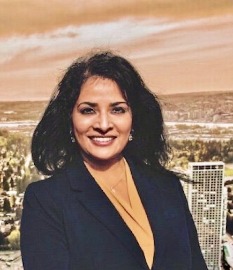 A South Asian woman smiles at the camera with a city and river behind.