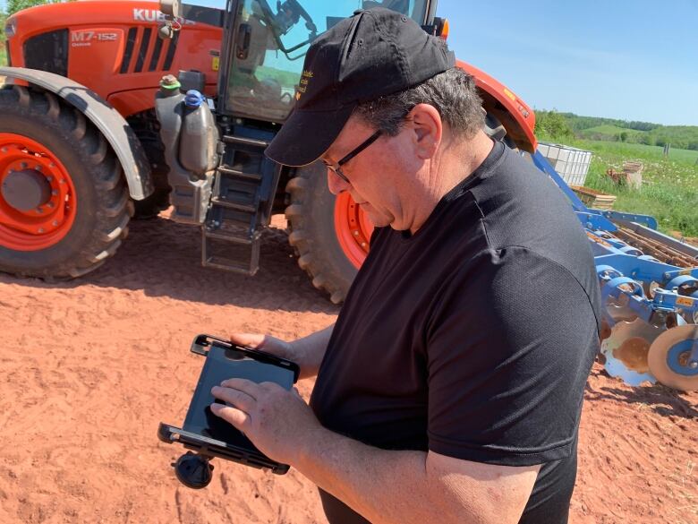 Alan Miller stands beside his tractor with the tablet he uses to program his fertilizer applicator. 