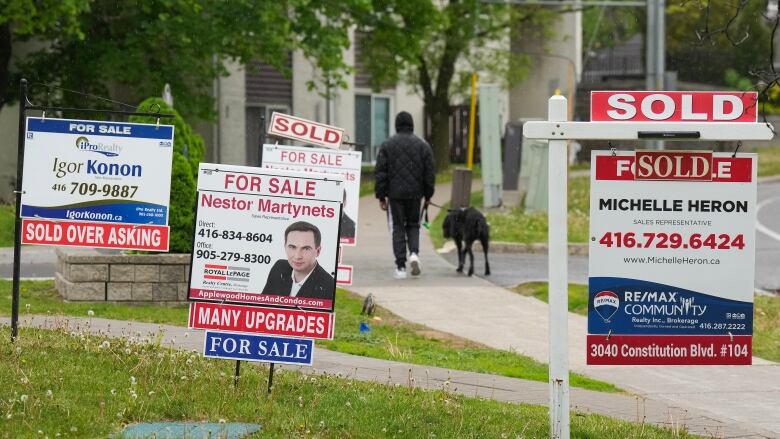 A person walks past multiple for-sale and sold real estate signs in Mississauga, Ont.