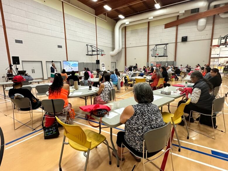 A gymnasium filled with people look to the speaker.