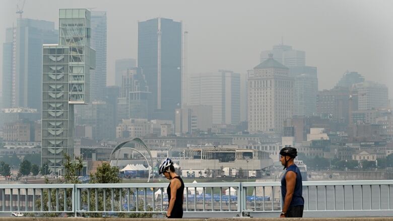 Montreal skyline in the background covered by a haze of smoke. Two people in the forefront are exercising outdoors. 