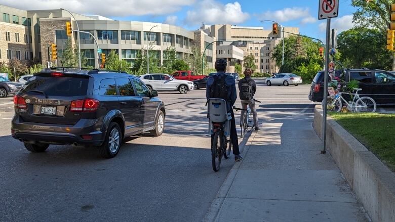 A pair of cyclists await a green light to cross College Drive in front of the University of Saskatchewan on a traffic-heavy morning.