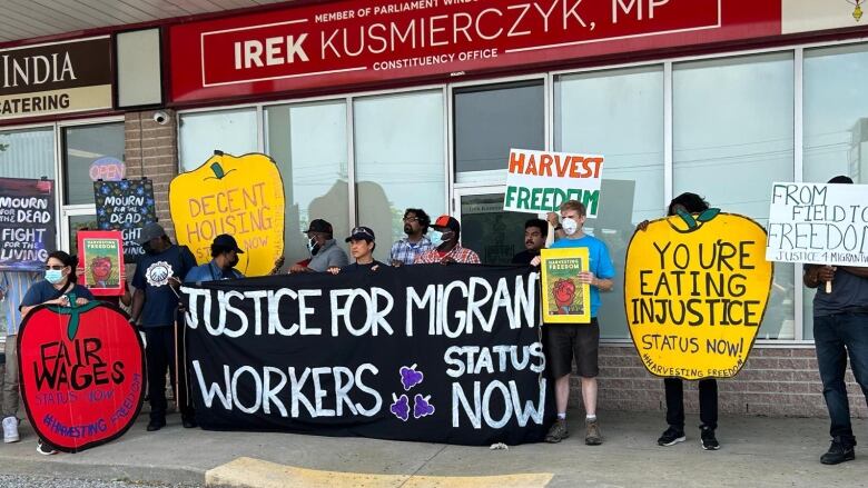 A group of protesters holding signs stand in front of an office.