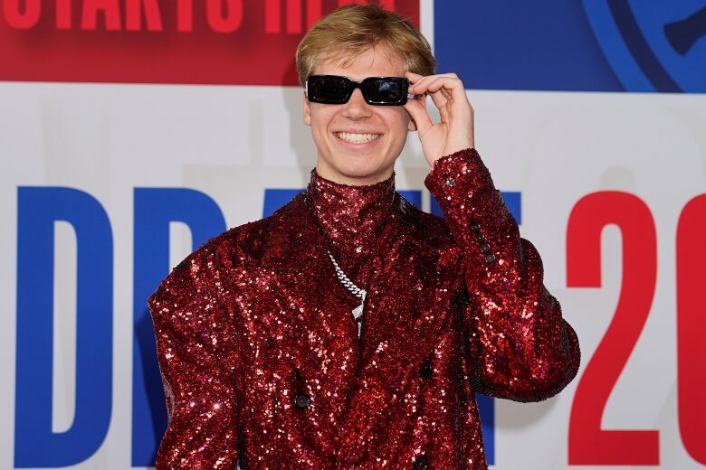 A man in a shiny red suit and sunglasses smiles.