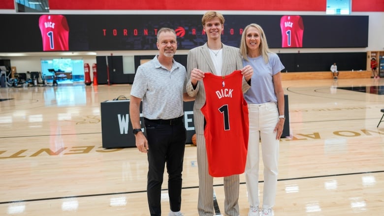 A basketball player holds a jersey as he's flanked by his parents.