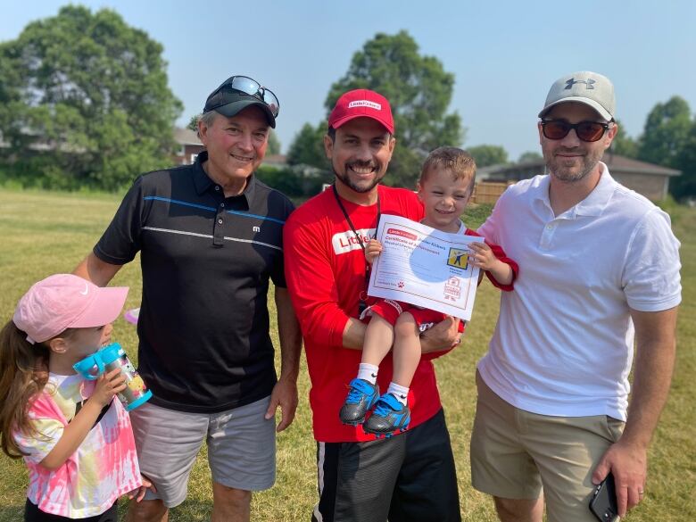 A man holding a small child who has a diploma in his hands. There are two other men, and a little girl posing in the photo.