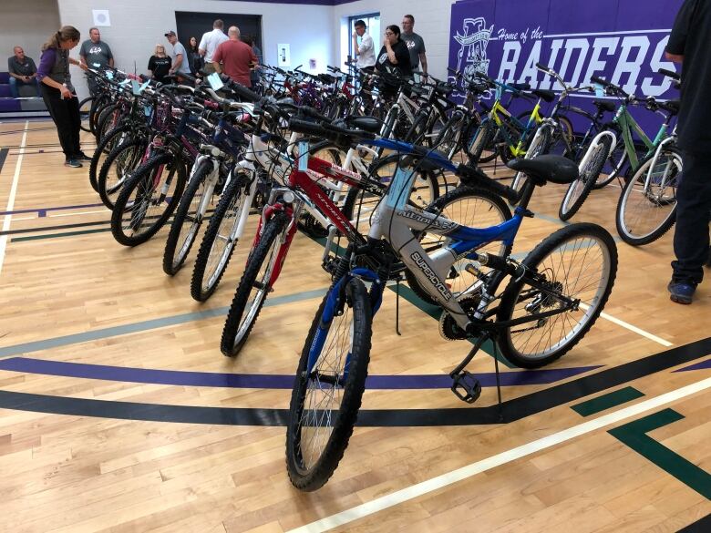 A bunch of bicycles lined up in a school gym.