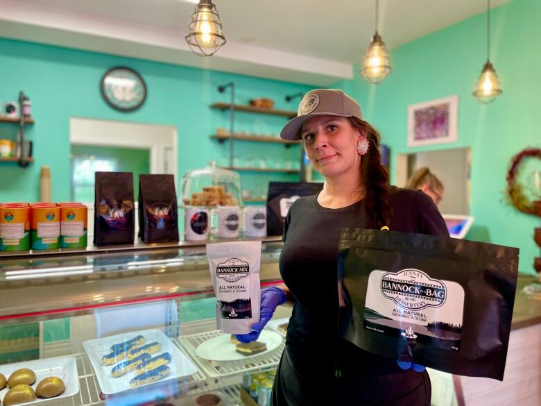 A woman holding two bags of food products and standing in front of a dessert show glass.