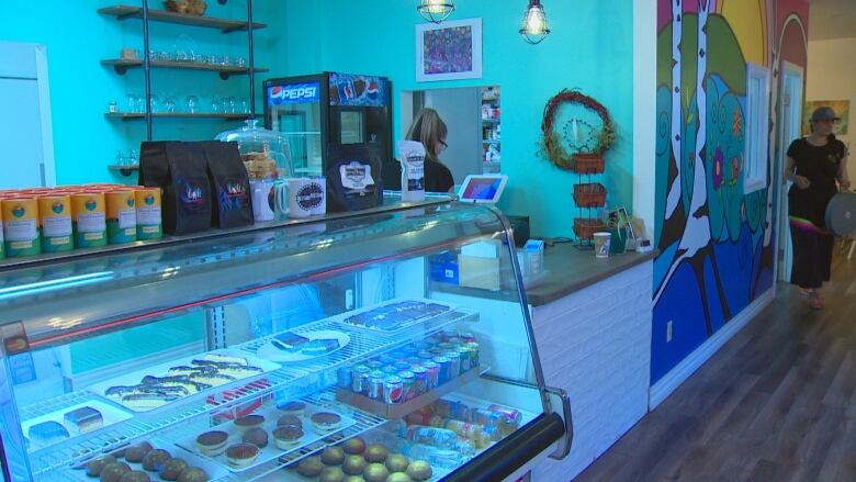 Inside a restaurant a woman is standing behind a snack show glass and another woman is walking by.