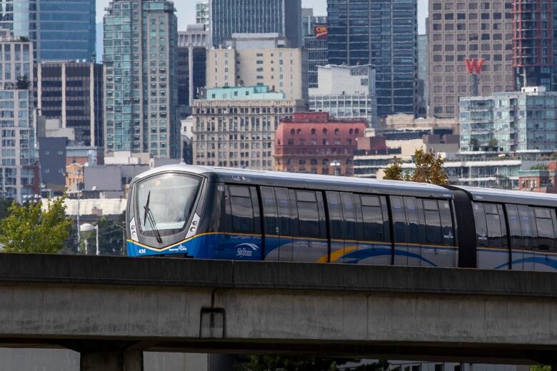 A light rail train passing in front of a downtown skyline.