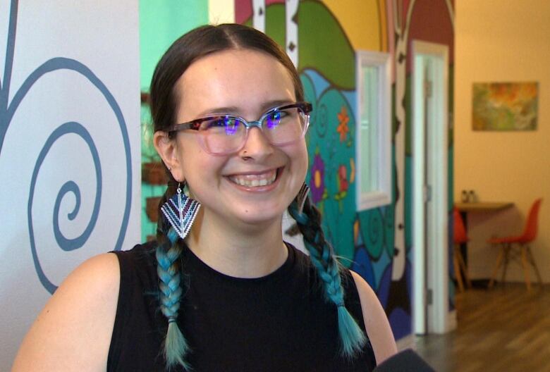 A young woman with a blue colored hair standing in front of a graffiti wall.