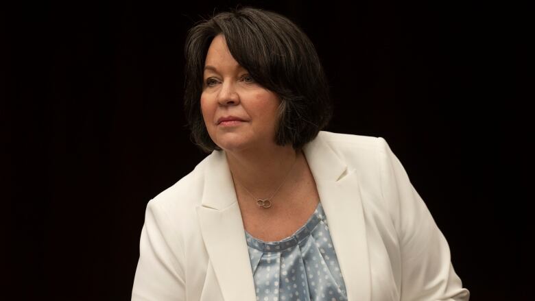 A woman in businesswear leans forward, against a black background.