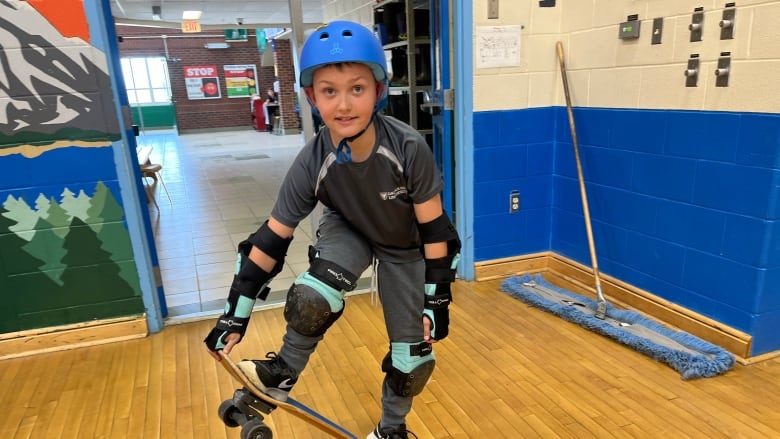 A young boy in a helmet poses on a skateboard.