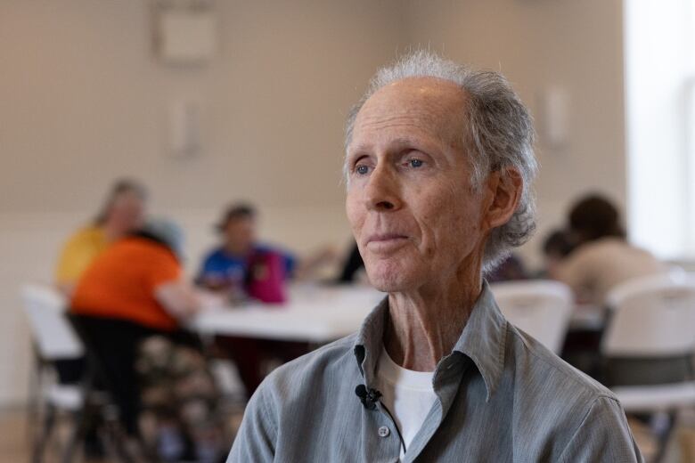 An older person in a grey shirt looks contemplatively in a busy lunchroom. 