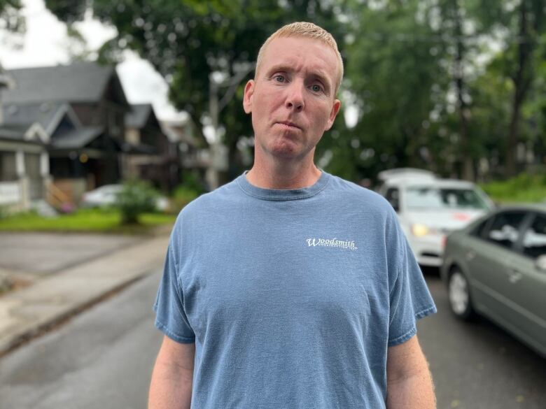 A man in a Woodsmith t-shirt stands on a street.