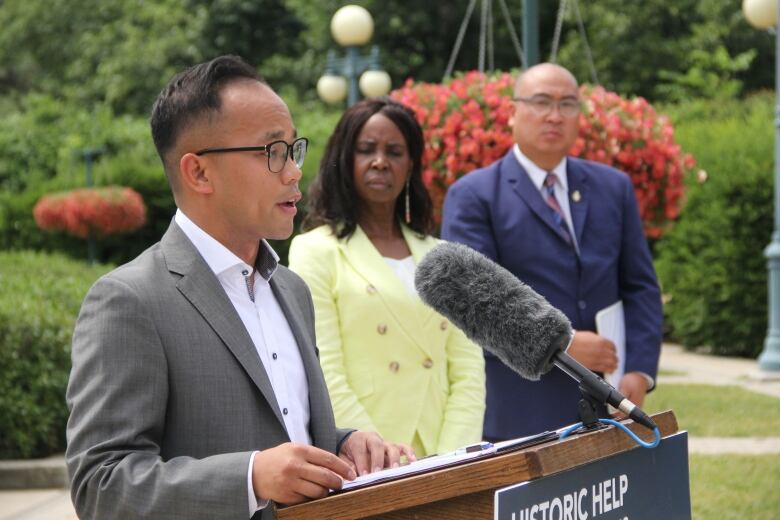 A man speaks at a news conference, while flanked by two government cabinet ministers.