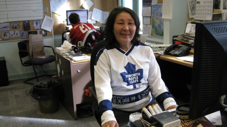 A woman in an office sits at a desk in front of her computer, wearing a Toronto Maple Leafs jersey.