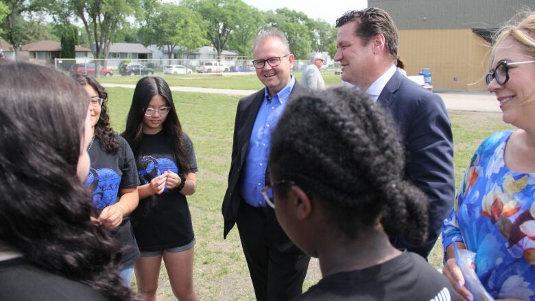 MLAs and students stand in a circle and talk amongst themselves. 