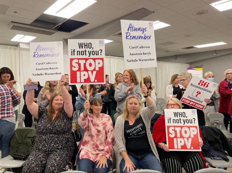 People hold signs in a meeting room that remember victims of intimate partner violence.