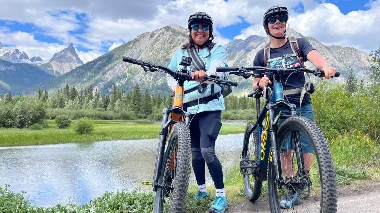 Two people with bicycles, with mountains in the background.