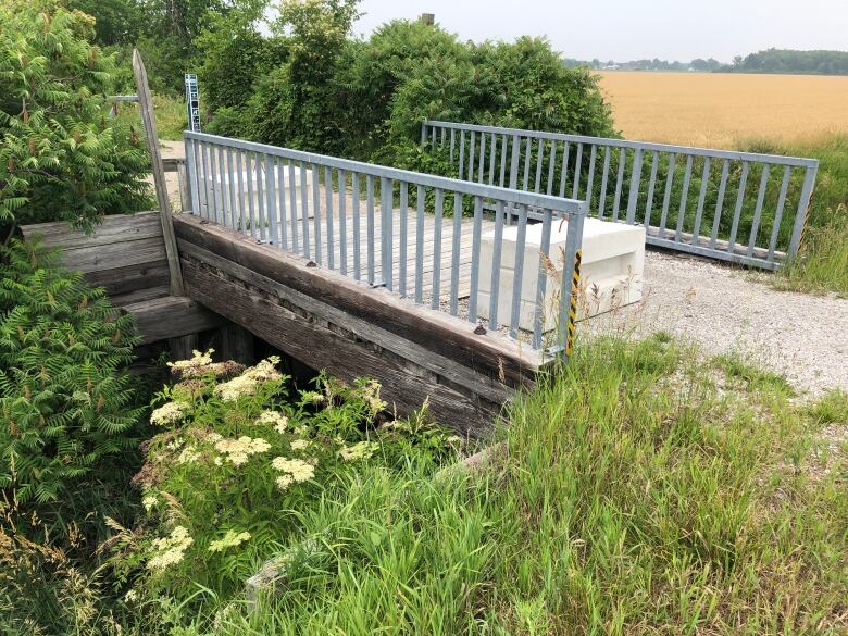 A small wooden bridge on a dirt trail with a farmer's field in the background.