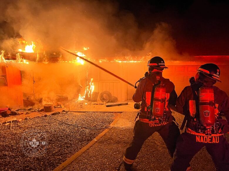 Firefighters are holding a hose to splash water into a fire in a house.