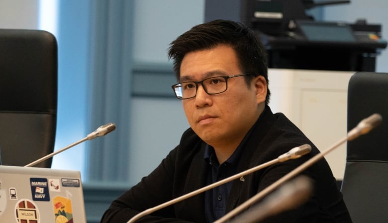 A man sits in front of a laptop and a microphone.