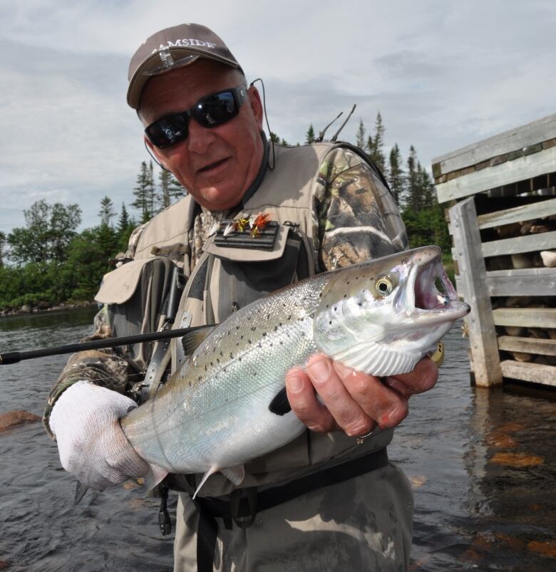 A man in sunglasses and camouflage fishing gear holds up a fish.