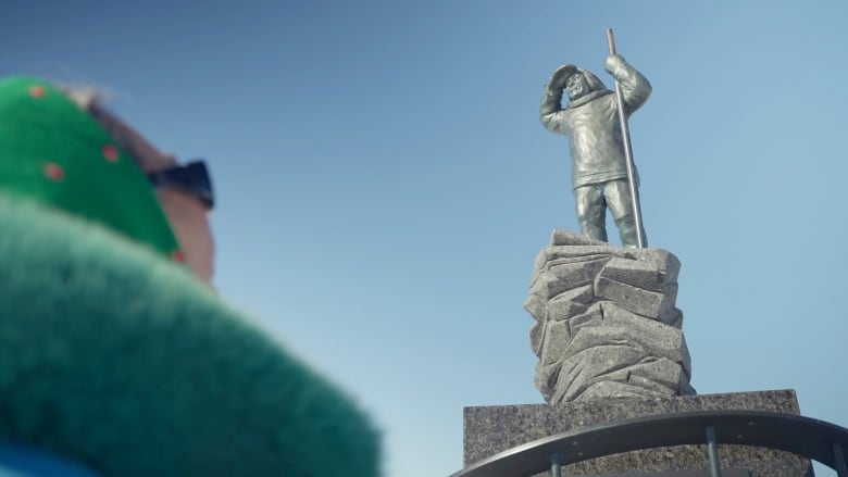 Elisapie Nutuara visits a monument in Inukjuak showing an Inuk man looking out to sea.