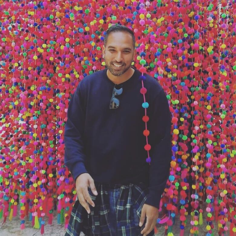 A man pictured among a curtain of colourful orbs on strings. 