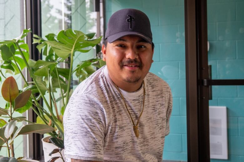 A man poses in front of a green plant.