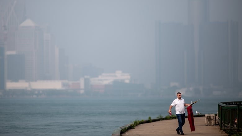 A man walks along the Windsor riverfront with the Detroit skyline in the background