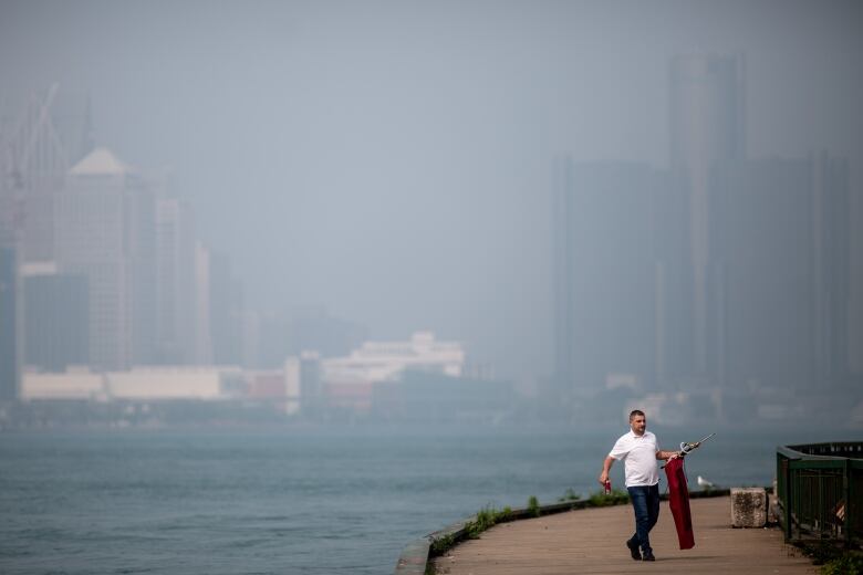 A man walks along the Windsor riverfront with the Detroit skyline in the background