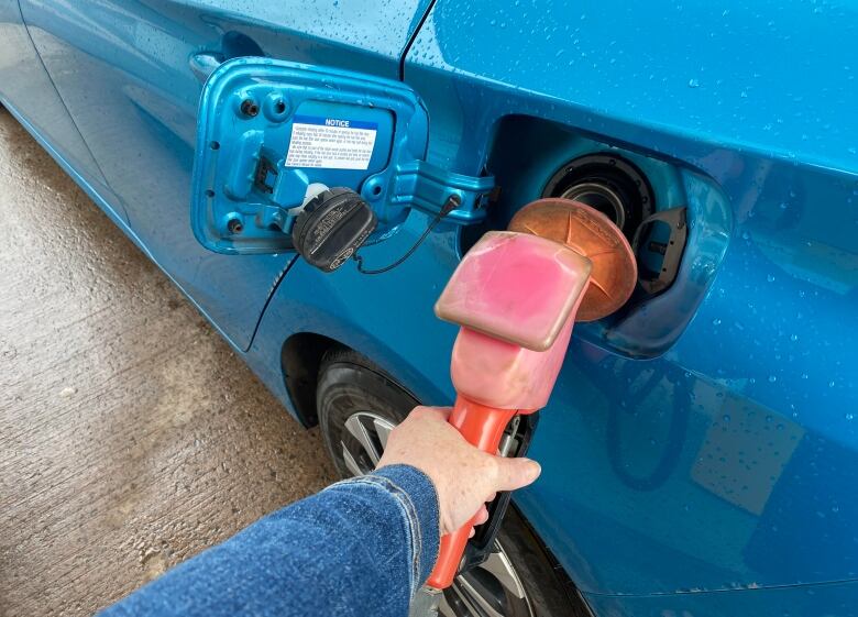 Hand holds gas pump nozzle to tank of blue car. 