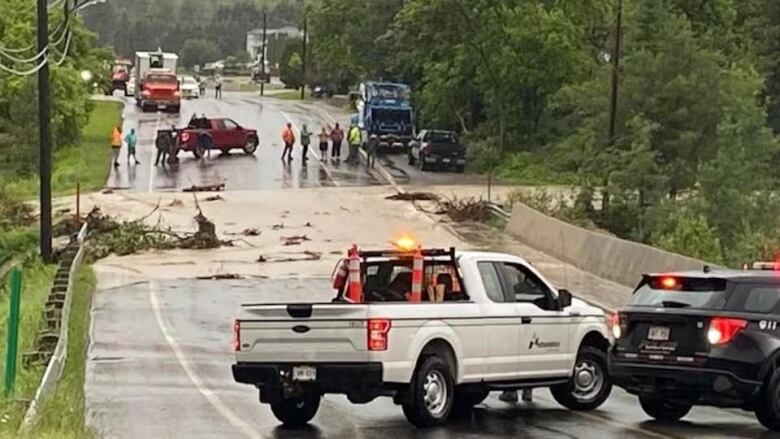 A washed out road with people parked on either side of the washed out section.